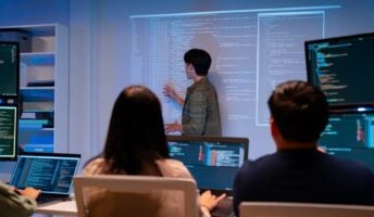 Workers in dark room with code on wall and on laptops