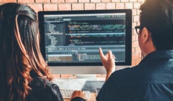 Man and woman looking at code on a laptop sat at a desk. Source: Tech.co Testing
